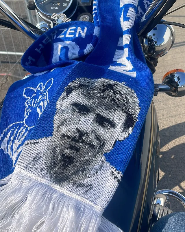 Blau-weißer Fanschal mit dem Porträt von Michael Tönnies auf einem Motorradtank