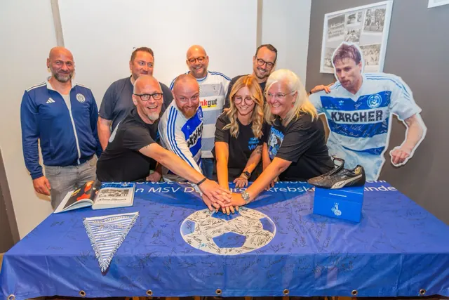 Acht Menschen legen ihre Hände auf ein blaues, vielfach signiertes MSV-Fahnentuch, daneben ein Aufsteller von Michael Tönnies im Kärcher-Trikot und ein signierter Fußballschuh